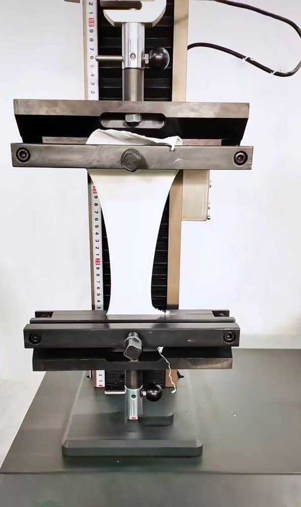 A professional lab fabric stretch and recovery test in progress, ensuring the performance fabrics used by Maes for yoga pants meet strict four-way stretch and squat-proof standards.