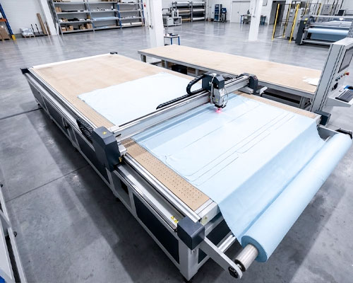 A high-precision industrial automatic fabric cutting machine processing a roll of light blue textile for activewear manufacturing.