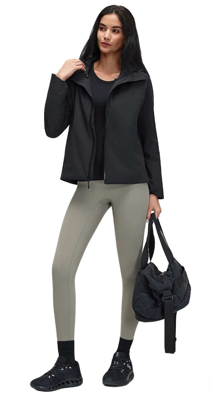 A professional showcase of a female model wearing a black cut-and-sew performance windbreaker jacket, grey high-waisted leggings, and carrying a matching athletic gym bag.