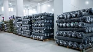 Industrial supply of breathable black UV protection fabrics wrapped in plastic, prepared for the cut and sew process of custom sun shirts.