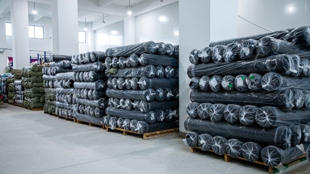Industrial supply of breathable black UV protection fabrics wrapped in plastic, prepared for the cut and sew process of custom sun shirts.